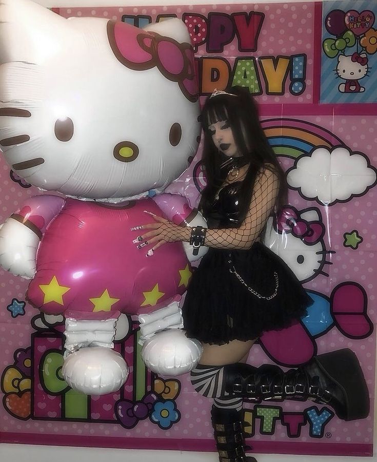 a woman standing next to a giant hello kitty balloon in front of a pink wall