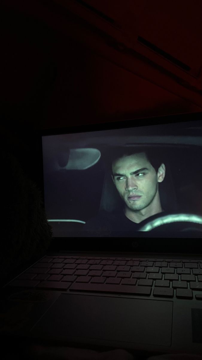 a laptop computer sitting on top of a desk in front of a screen with a man's face