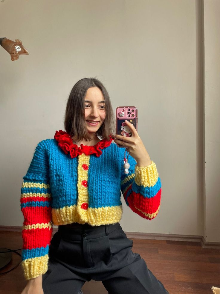 a woman sitting on the floor taking a selfie with her cell phone wearing a colorful sweater