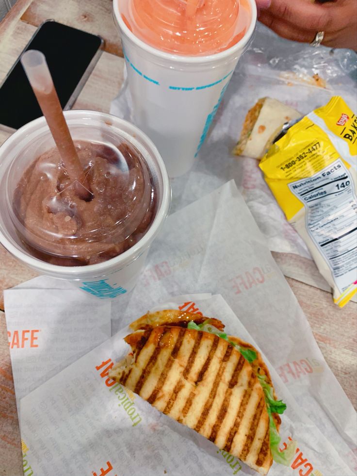 there is a sandwich and ice cream on the table next to each other with two drinks