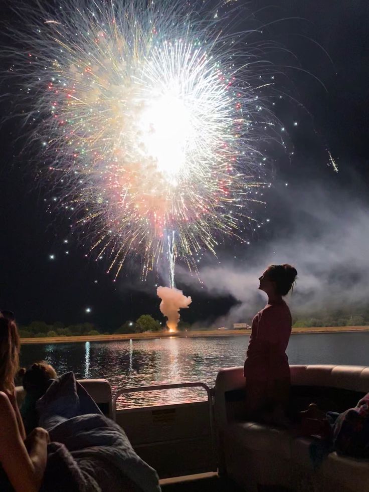 people sitting on a boat watching fireworks go off in the sky over water at night