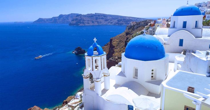 the blue domes and white buildings are on the cliff above the water's edge