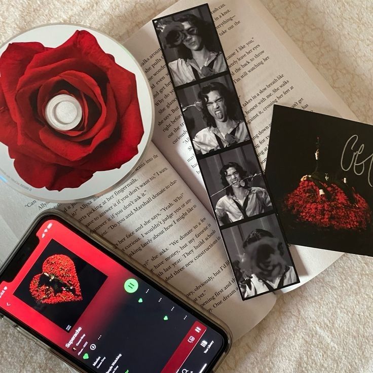 a cell phone sitting on top of an open book next to a red rose and cd