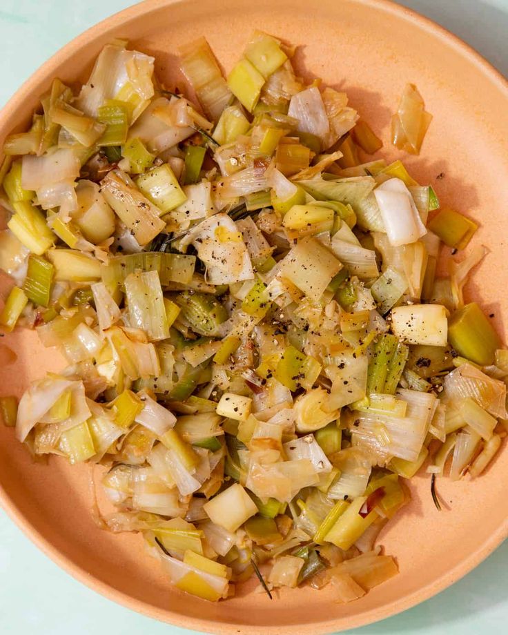 an orange bowl filled with chopped vegetables on top of a blue tablecloth next to a fork