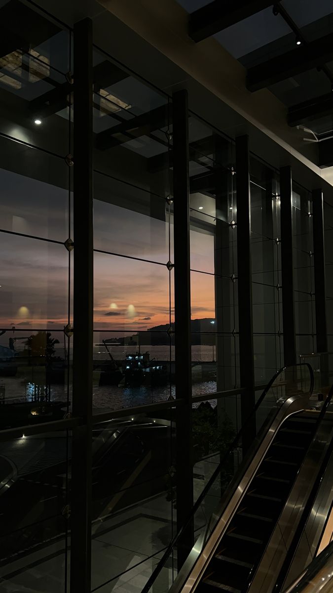 an escalator in front of a large window at night with the sun setting