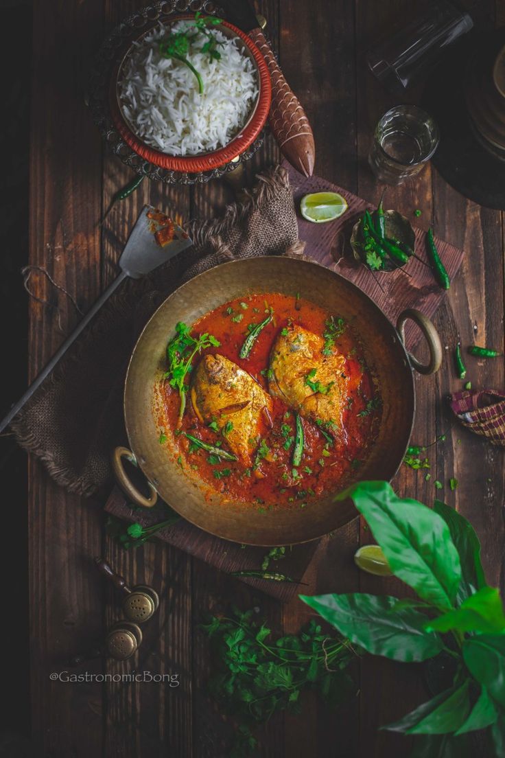 some food is in a brown bowl on a wooden table next to rice and green leaves