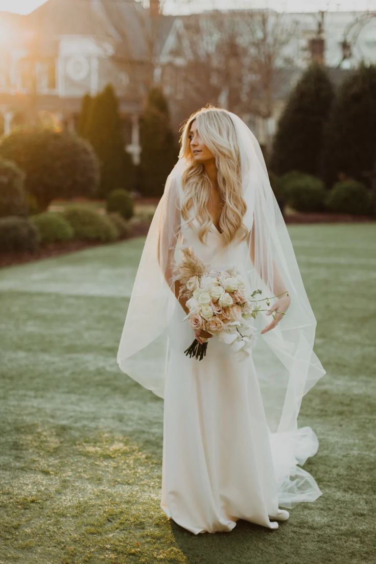 a woman in a wedding dress is standing on the grass with her veil over her head