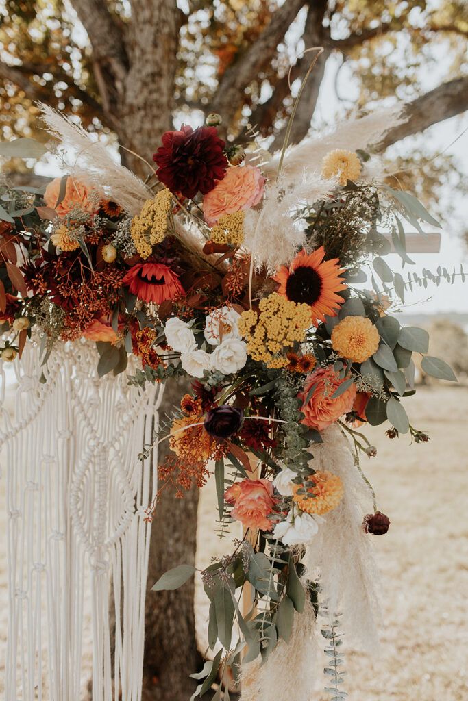 a wedding arch with flowers and feathers hanging from the tree in front of an open field