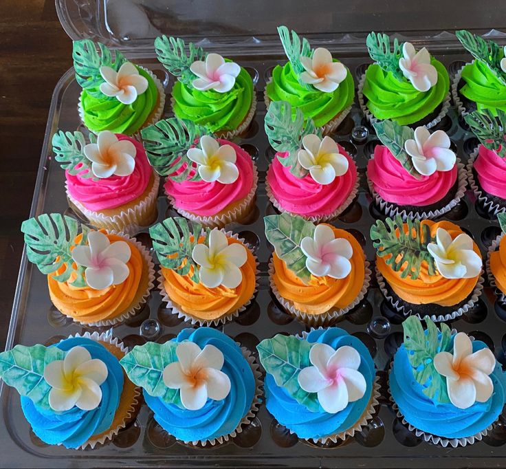 cupcakes decorated with colorful frosting and flowers on a plastic tray, ready to be eaten