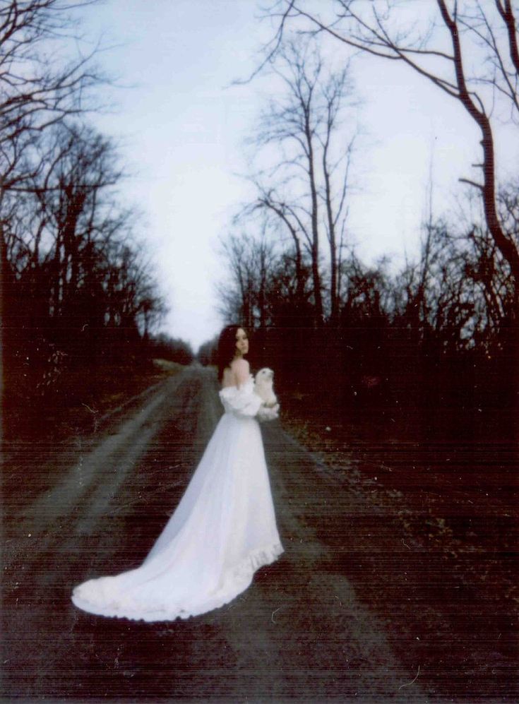 a woman in a long white dress standing on a road