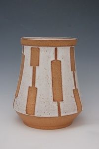 a white and brown vase with lines on the outside, sitting on a gray surface