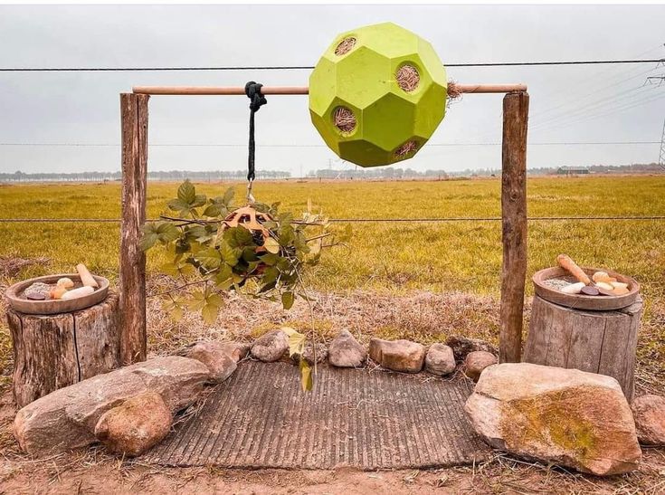 a large green object hanging from a wooden fence in the middle of a grassy field