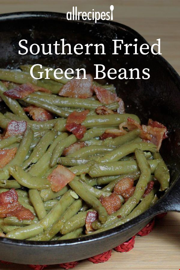 green beans with bacon in a frying pan on a wooden table next to a red napkin