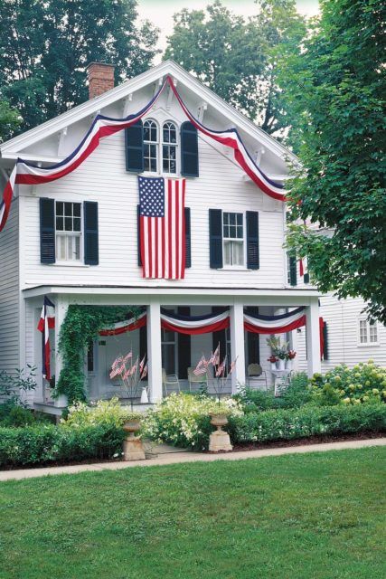 a white house with an american flag on it's roof and bushes in the front yard