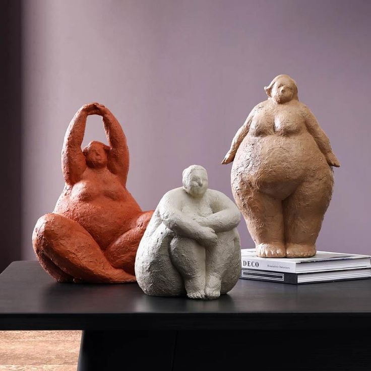 three clay sculptures sitting on top of a black table next to books and a purple wall