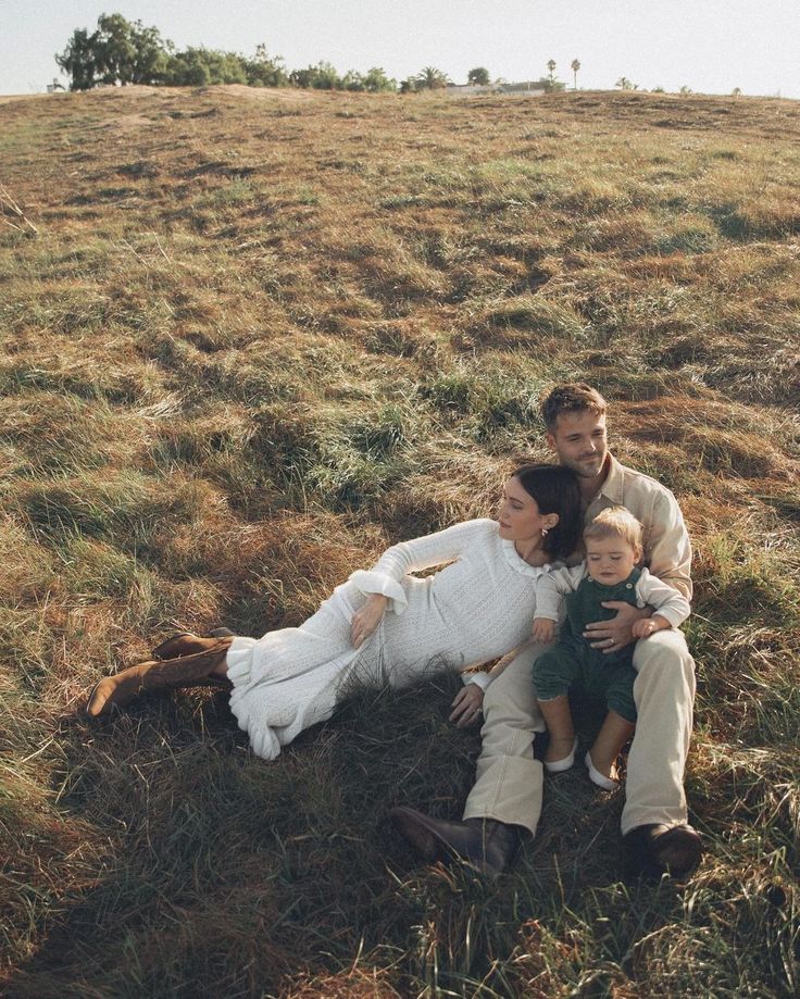 a man, woman and child are laying in the grass on a hill with their arms around each other