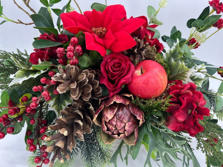 an arrangement of flowers, apples and greenery