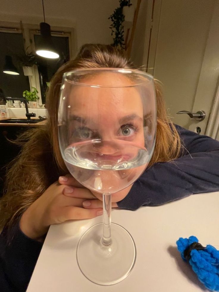 a woman sitting at a table with a wine glass in front of her and a blue object behind her