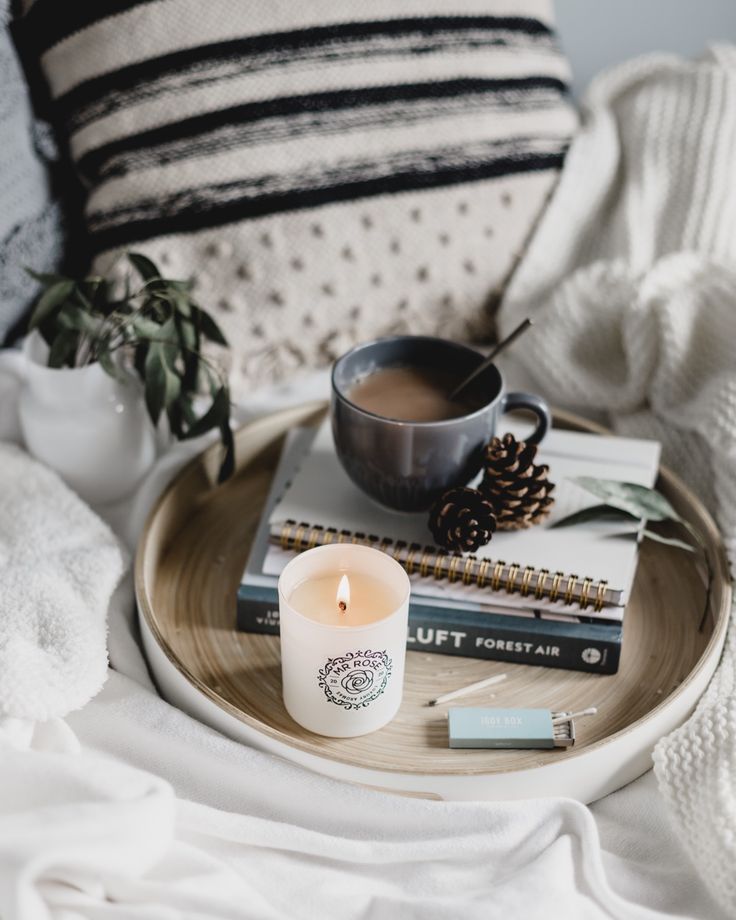 a cup of coffee and some books on a tray next to a candle with a spoon