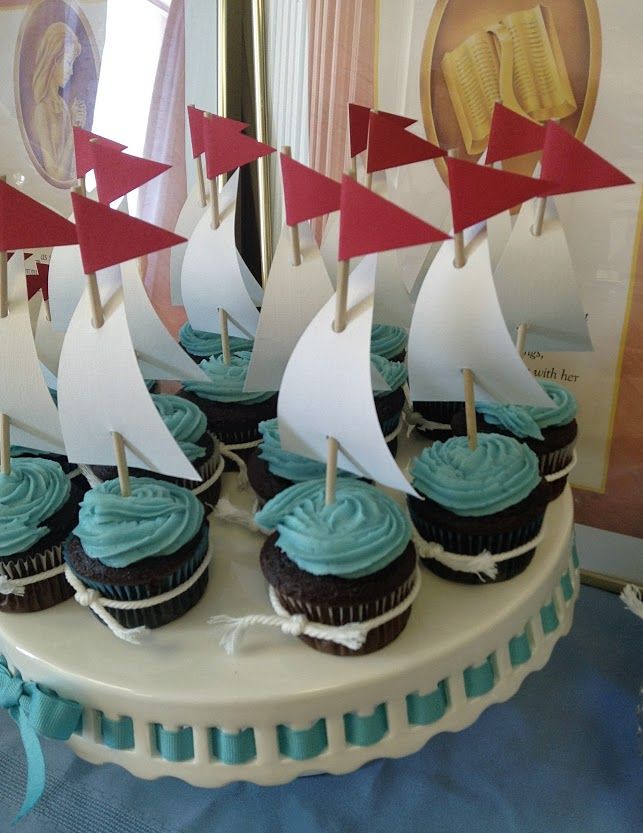 cupcakes with blue frosting and sailboats on them are sitting on a cake plate