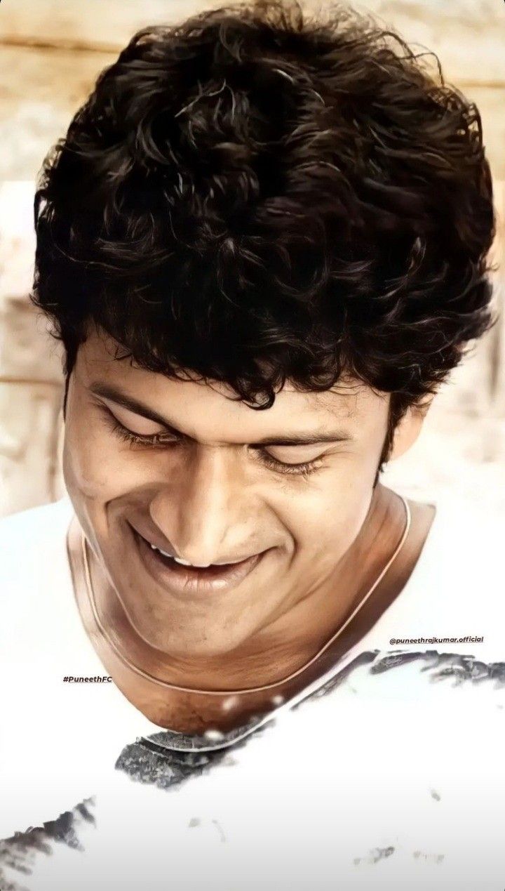 a close up of a person wearing a white shirt and black curly hair with a smile on his face