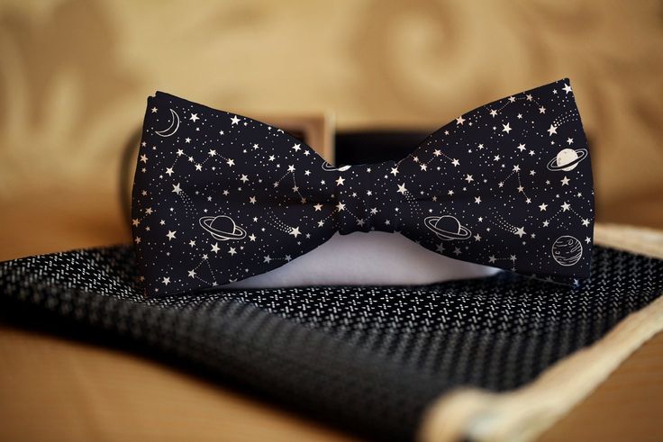 a black bow tie with white stars and planets on it is sitting on a table