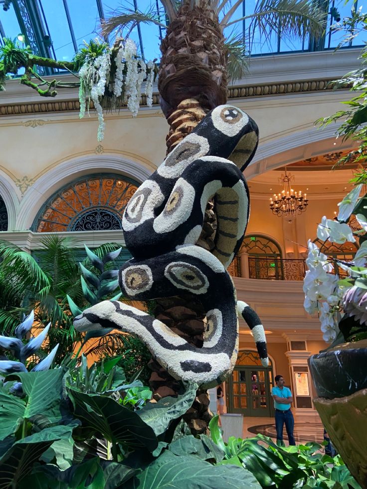 a large snake statue in the middle of a building with plants and trees around it