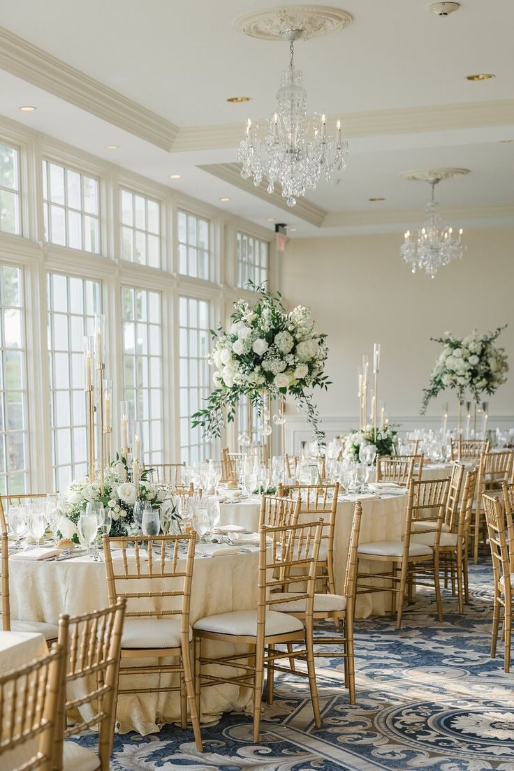 the tables are set with white flowers and greenery for an elegant wedding reception in front of large windows