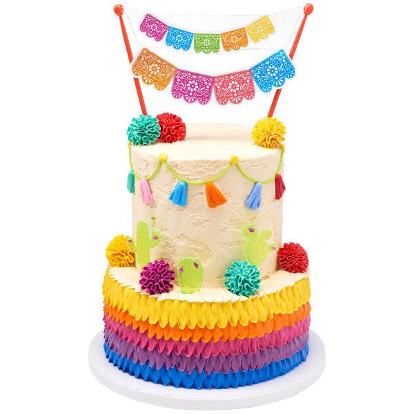 a multi - colored cake decorated with pom poms and streamers on top