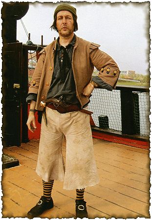 a man dressed in pirate garb standing on a deck with his hands on his hips