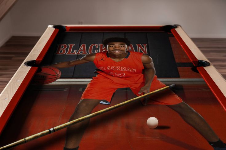 a man in an orange shirt is holding a stick and hitting a ball with a pool cue