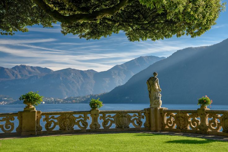 a statue is sitting on the edge of a balcony overlooking water and mountains in the distance