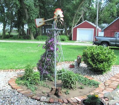 a windmill in the middle of a garden with rocks around it and flowers growing on top