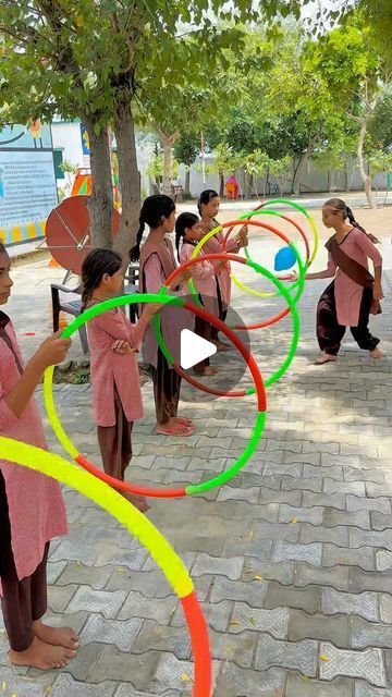 several children are playing with colorful hula hoops on the sidewalk in front of a tree