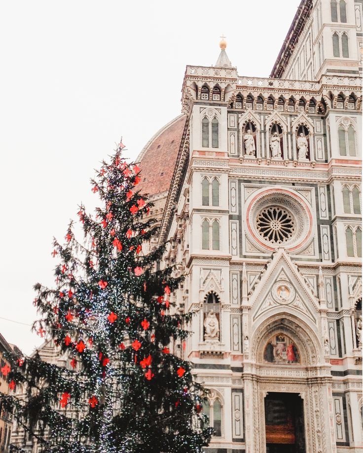 a large christmas tree in front of a church with red ornaments on it's branches