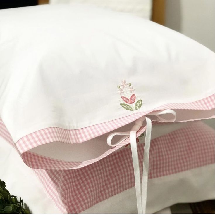 a white pillow on top of a pink and white gingham bed cover with a bow