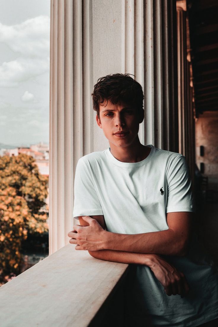 a young man leaning on a ledge with his arms crossed and looking at the camera