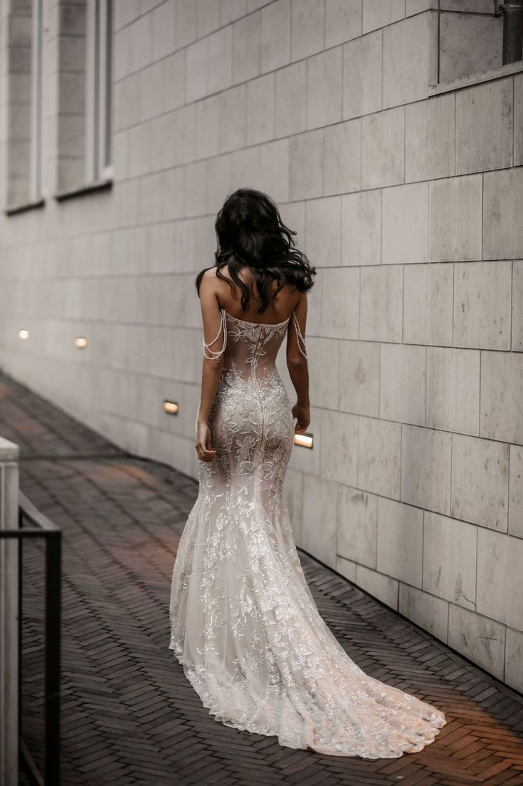 a woman in a wedding dress is walking down the street with her back to the camera