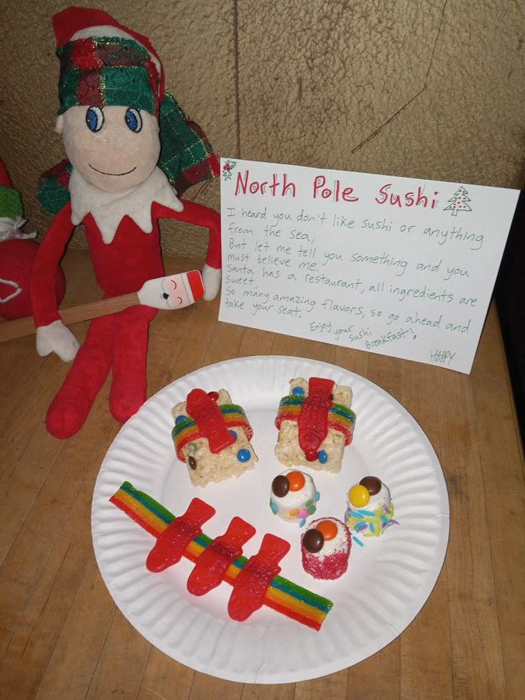 a paper plate topped with candy and marshmallows next to an elf holding a sign