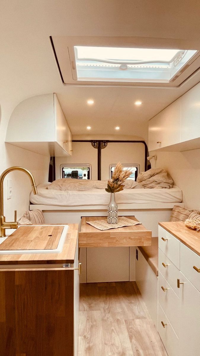 the interior of a camper with wood flooring and white walls, including a bed