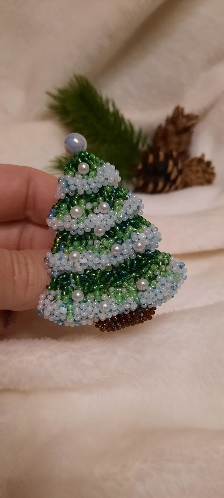 a hand is holding a beaded christmas tree ornament