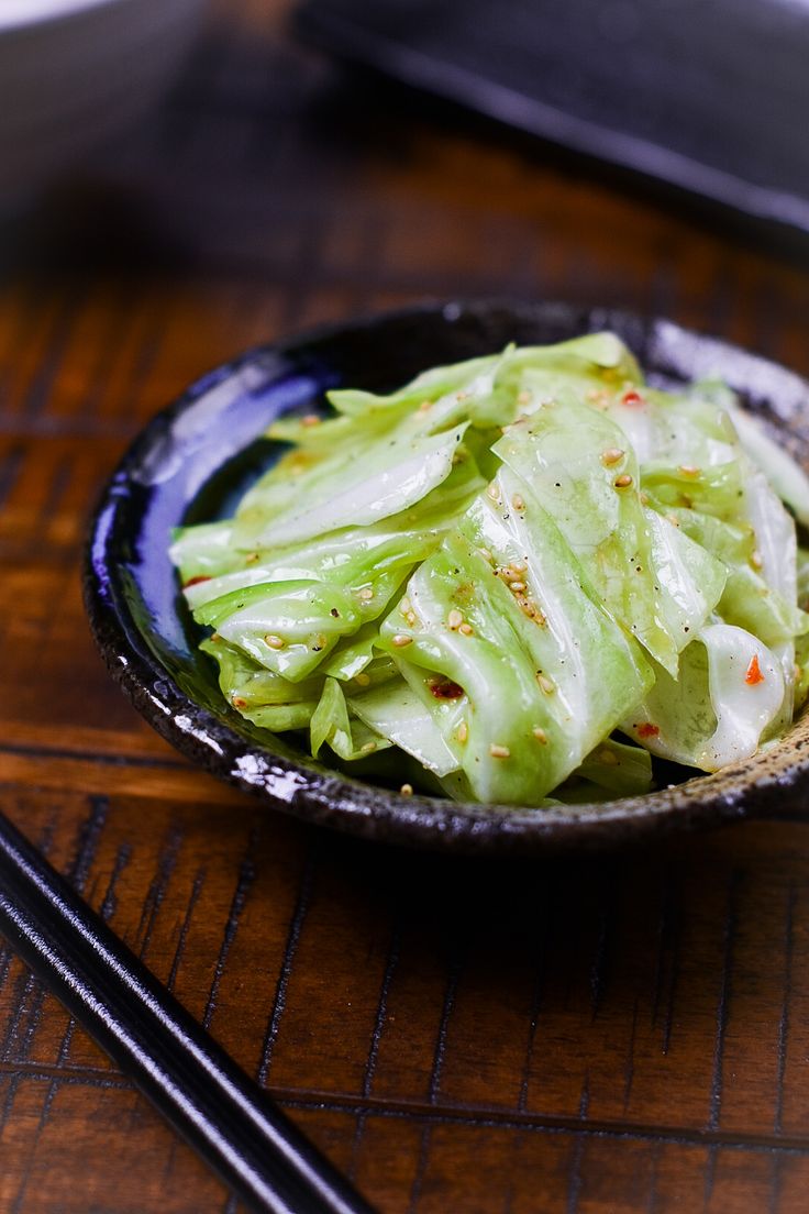 a black bowl filled with lettuce next to chopsticks