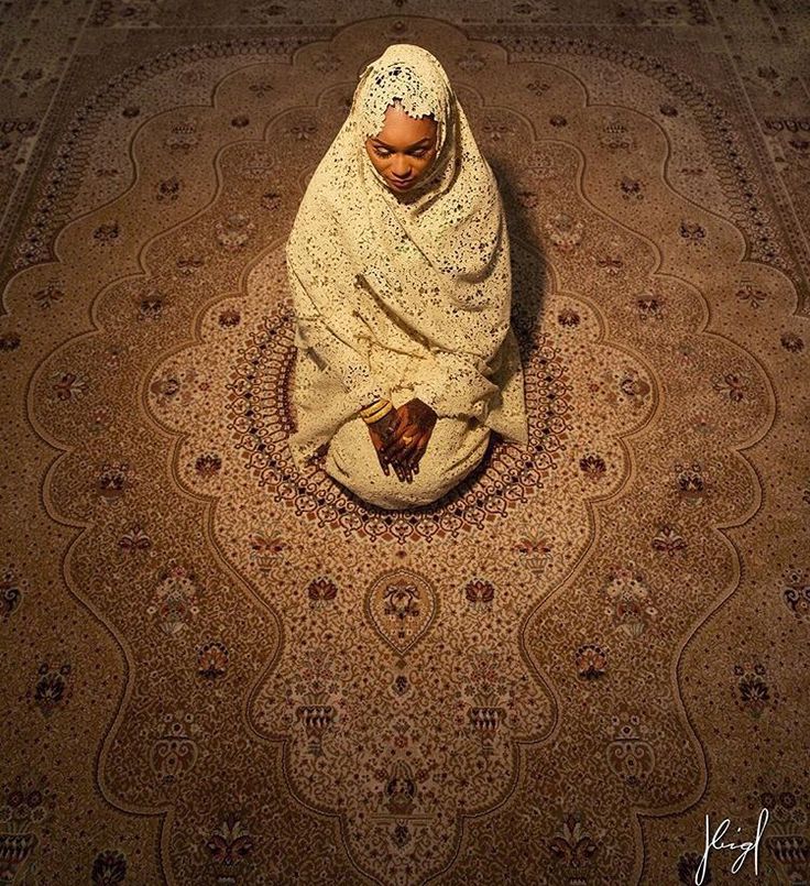 a woman sitting on top of a rug covered in a shawl over her head