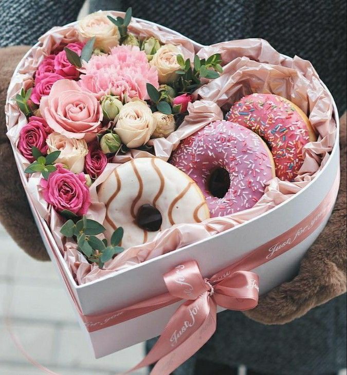 a person holding a heart shaped box filled with donuts and roses in front of a brick wall