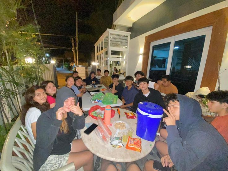 a group of young people sitting around a table eating food and drinking beverages at night