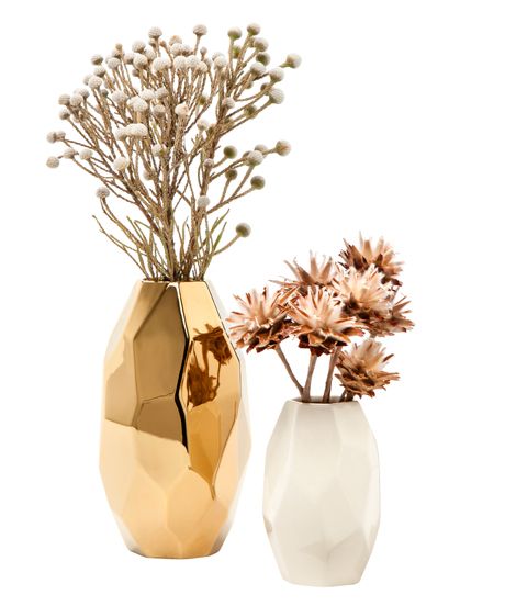 two vases with dried flowers in them on a white background, one gold and the other white