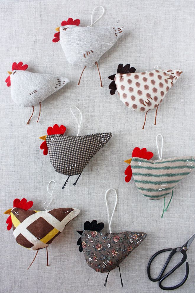 several different types of chicken ornaments hanging from clothes pins on a white tablecloth with scissors