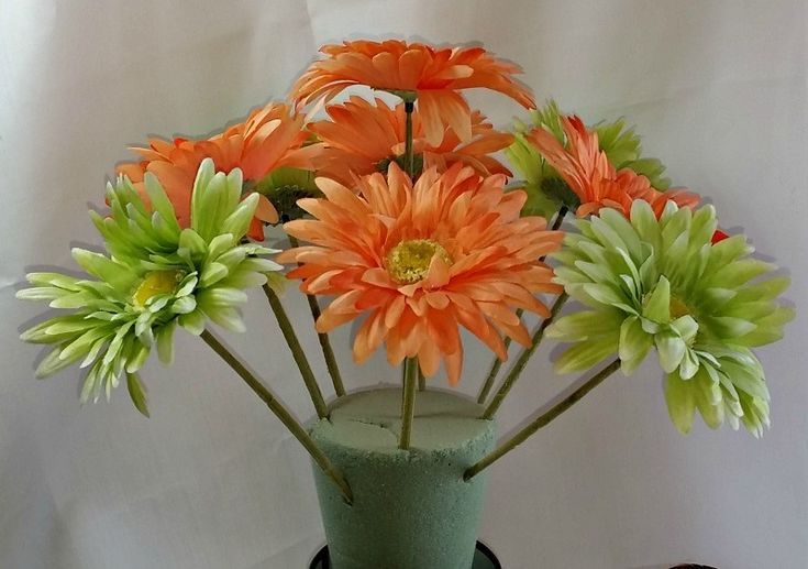 an arrangement of flowers in a green vase on a white tableclothed surface,