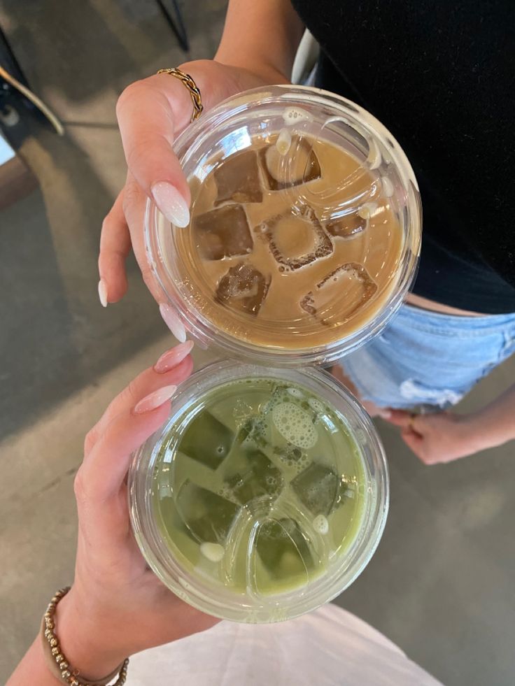 two people holding up cups with ice cubes in them and one has green liquid