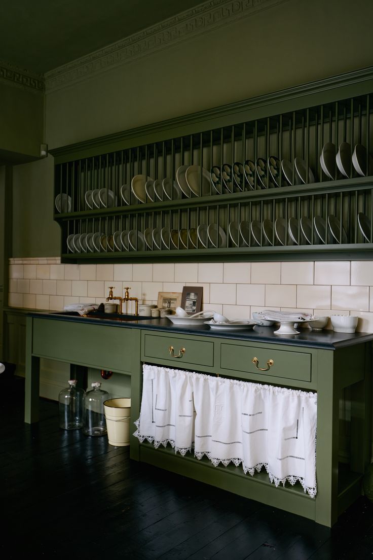 a kitchen with green cabinets and white dishes on the counter top, along with black wood flooring